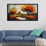 A large horizontal framed impressionist canvas painting of an autumn countryside landscape with a vibrant orange tree and a reflective river puddle, hanging on a wall above a blue sofa with a teal pillow.